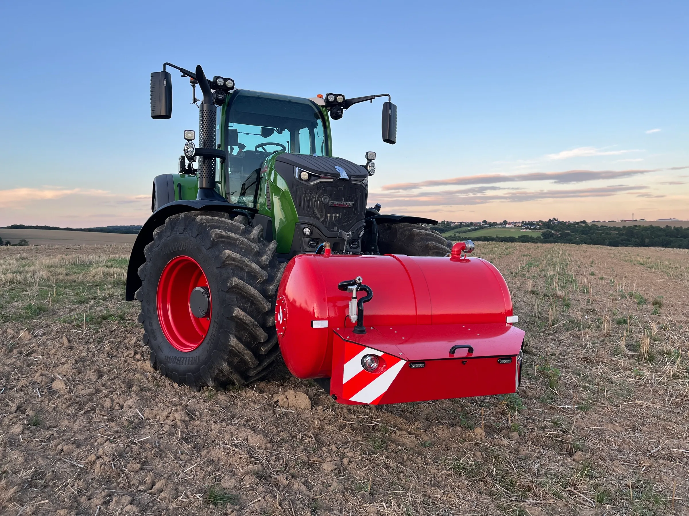 Traktor Fendt s hasicí nástavbou HYDROTANK na čelním tříbodovém závěsu na strništi za podvečerního světla