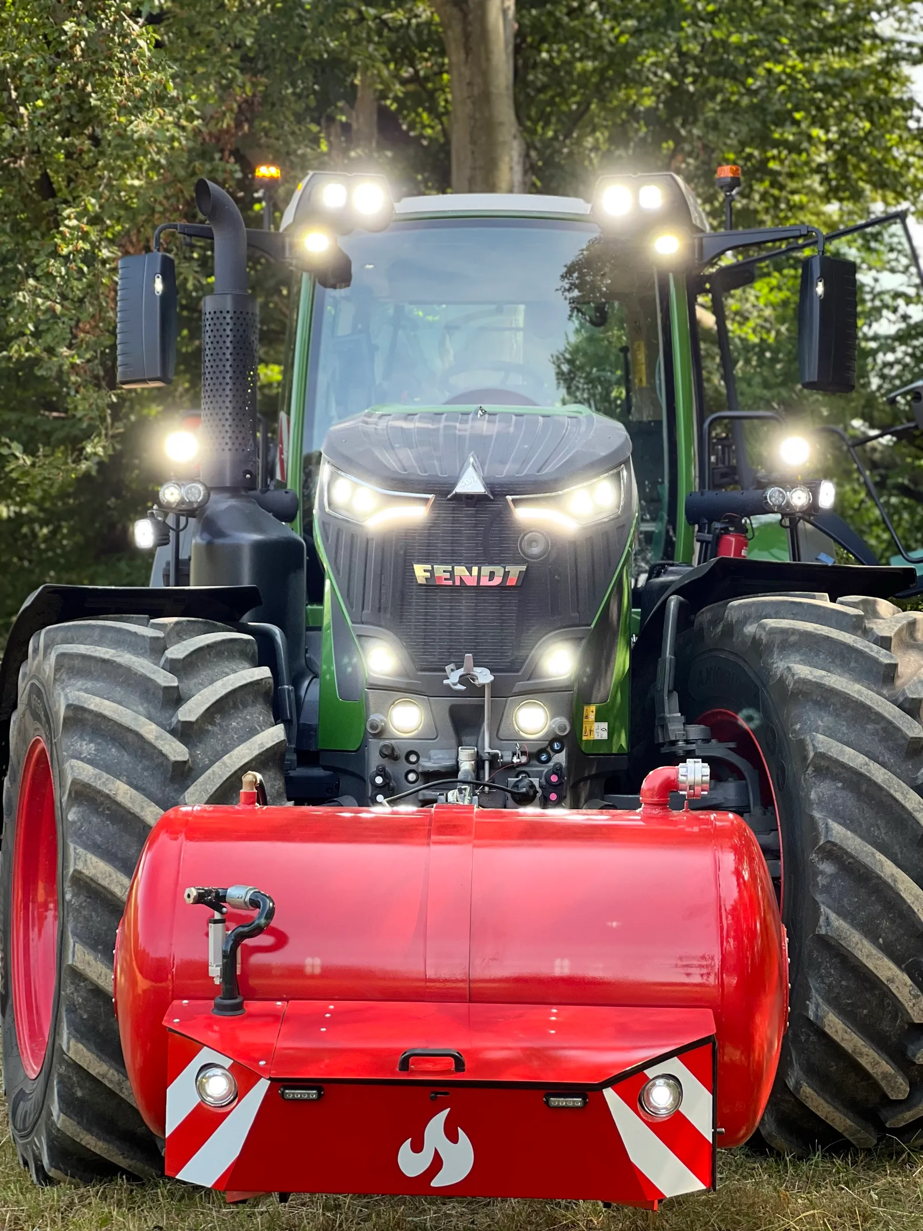 Traktor Fendt s Patronem a rozsvícenými pracovními světly za soumraku