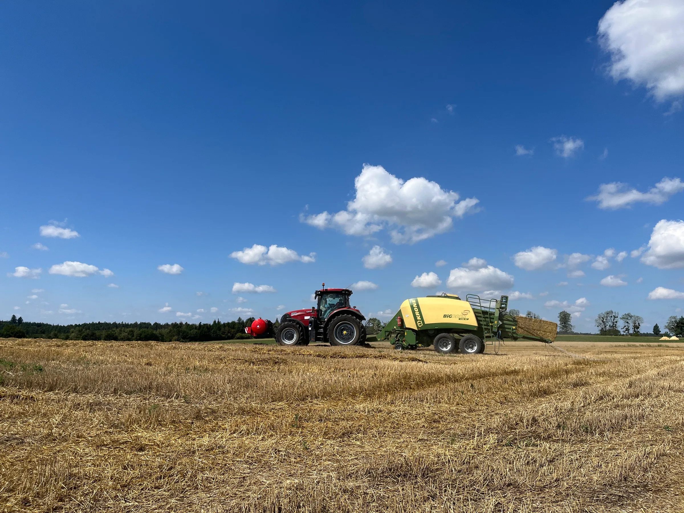 Traktor s nástavbou Patron a lisem na rozlehlém strništi pod modrou oblohou
