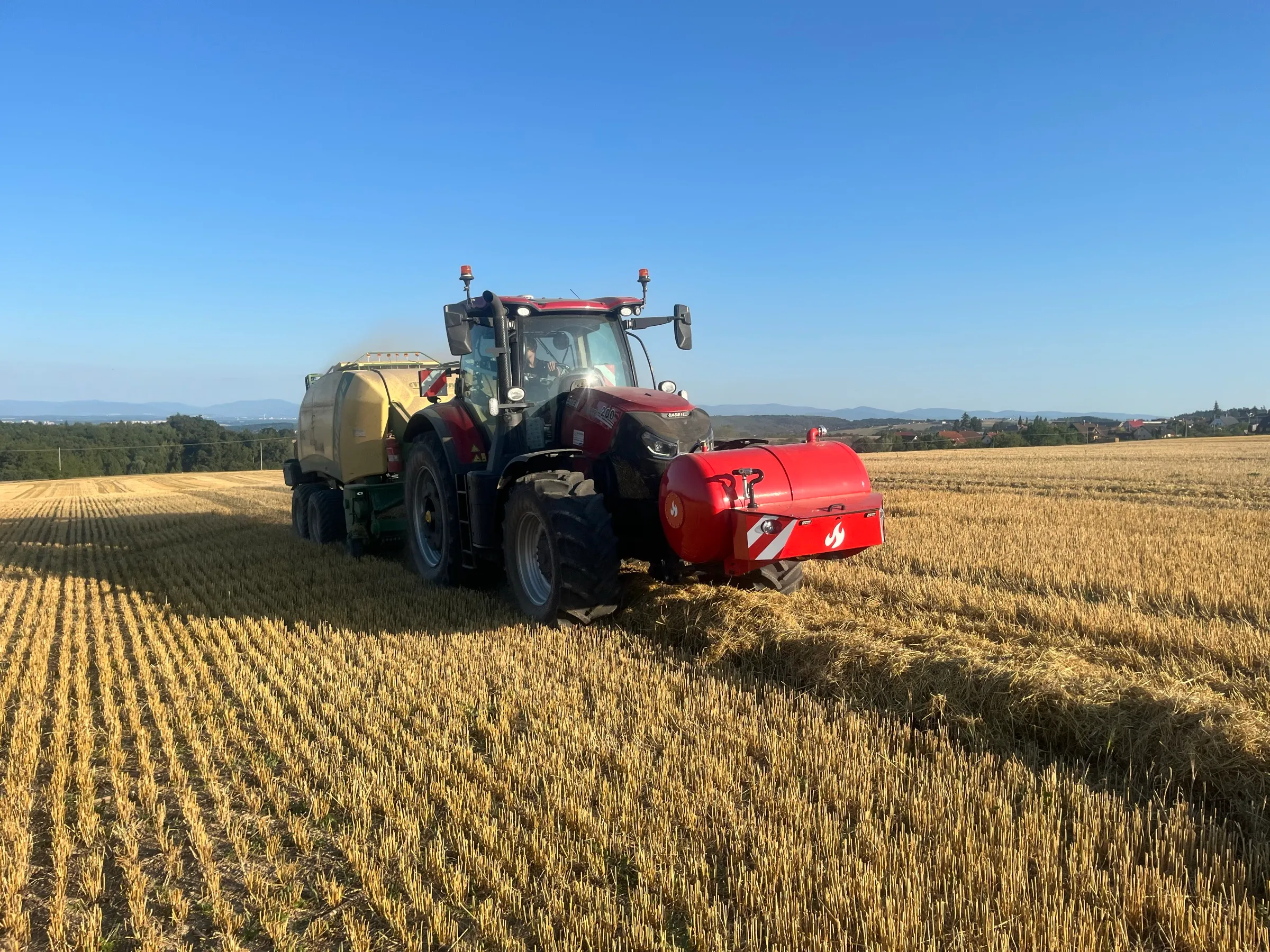 Traktor Case IH s nástavbou Patron a lisem na strništi za podvečerního světla